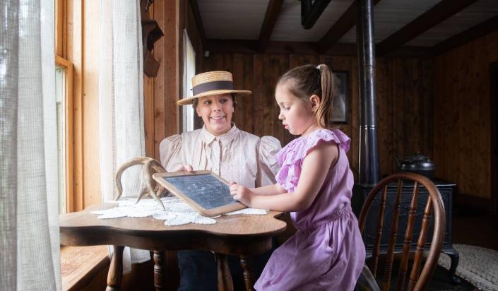 historically costumed interpreter helps young child to write on a slate
